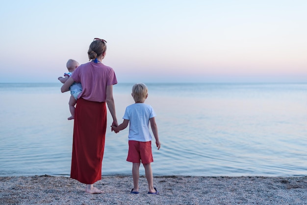 Jonge moeder wandelen op het strand met zoon en pasgeboren Moederschap en saamhorigheid concept