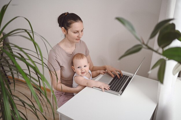 Jonge moeder werk studeren vanuit huis met laptop, kleine schattige peuter baby op schoot.