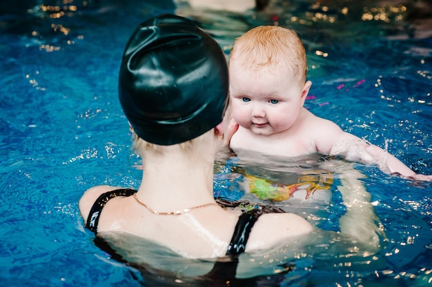 Jonge moeder, zweminstructeur en gelukkig meisje in peuterbad. leert baby-kind zwemmen. geniet van de eerste dag zwemmen in water. moeder houdt hand kind duiken voorbereiden. oefeningen doen