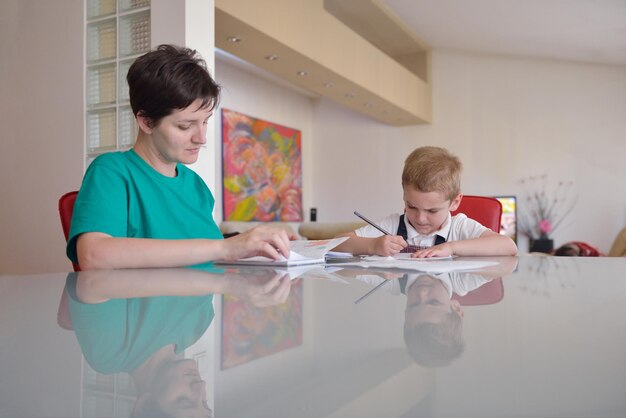 jonge moedervrouw die thuiswerk doet met een basisschooljongen thuis in de keuken