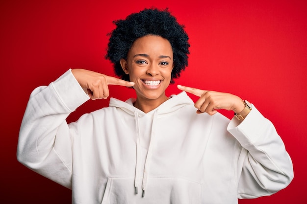 Jonge mooie Afro-Amerikaanse afro-sportvrouw met krullend haar die sportkleding draagt die vrolijk glimlacht en wijst met vingers, tanden en mond Tandheelkundig gezondheidsconcept