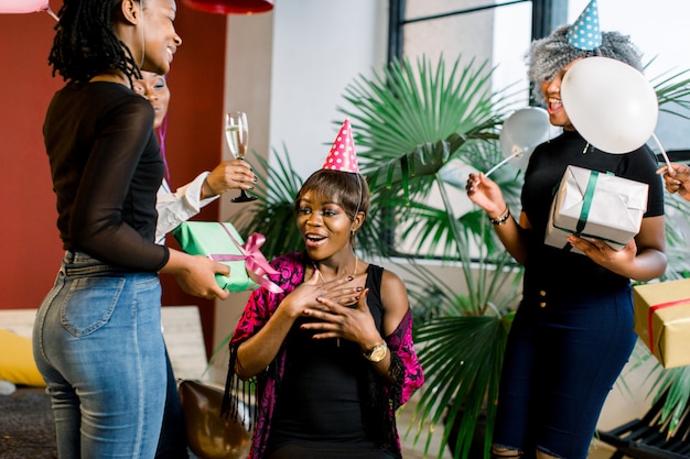 Jonge mooie afro-amerikaanse meisjes met ballonnen en hoeden vieren verjaardag en geven verjaardagscadeautjes.