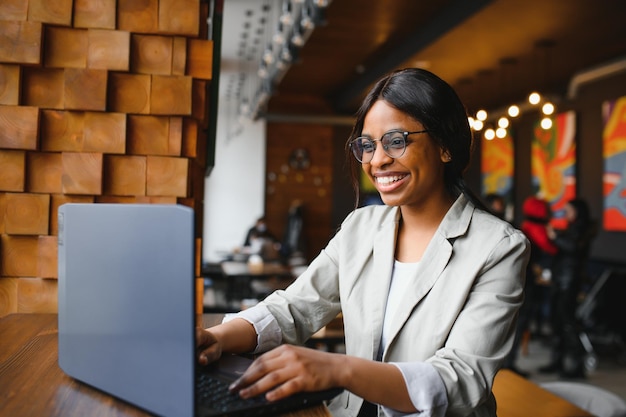 Jonge mooie Afro-Amerikaanse zakenvrouw die laptop gebruikt terwijl ze in café werkt