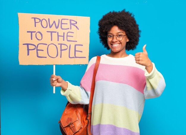 Jonge mooie afrovrouw die protesteert met een macht aan de mensenbanner