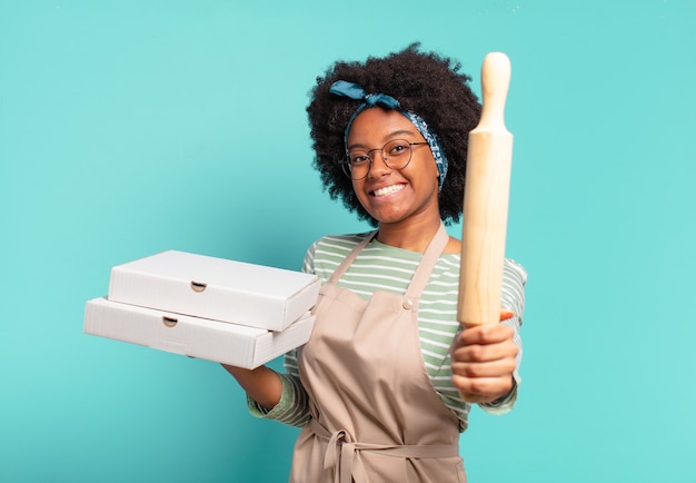 Jonge mooie afrovrouwenchef-kok met een deegroller en pizza's