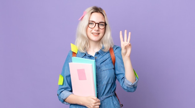 Jonge mooie albino-vrouw die lacht en er vriendelijk uitziet, met nummer drie. studentenconcept