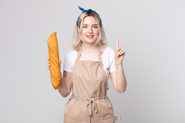 Jonge mooie albino-vrouw die lacht en er vriendelijk uitziet, nummer één toont met een broodbaguette