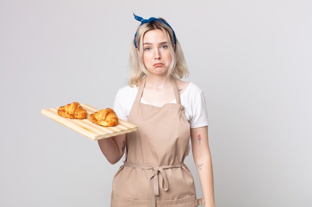 jonge mooie albino-vrouw die verdrietig en zeurt met een ongelukkige blik en huilt met een dienblad met croissants