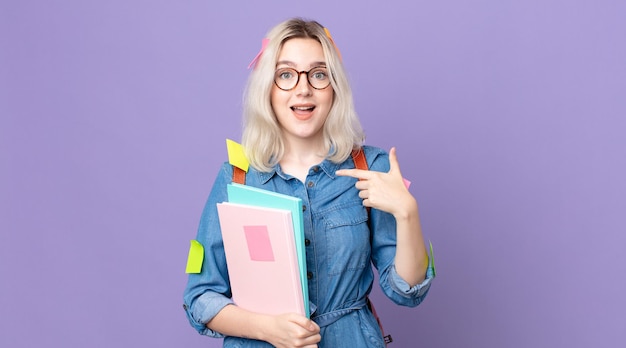 Jonge mooie albino-vrouw die zich gelukkig voelt en naar zichzelf wijst met een opgewonden studentenconcept