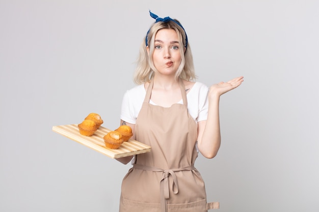 Jonge mooie albino-vrouw die zich verward en verward voelt en twijfelt met een dienblad met muffins