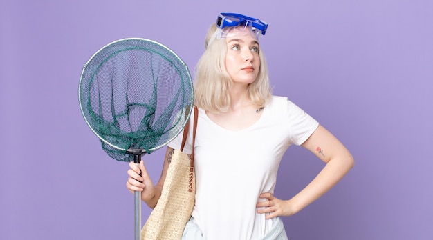 Jonge mooie albinovrouw die haar schouders ophaalt, zich verward en onzeker voelt met een veiligheidsbril en een visnet