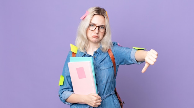 Jonge mooie albinovrouw die kruis voelt, duimen naar beneden toont. studentenconcept