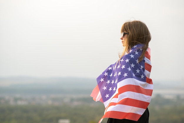 Jonge mooie amerikaanse vrouw met lang haar die op de wind van de V.S. op haar schouders zwaait en buiten staat en geniet van een warme zomerdag.