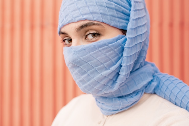 Jonge mooie arabische vrouw met haar gezicht verborgen achter blauwe hijab op zoek naar jou geïsoleerd