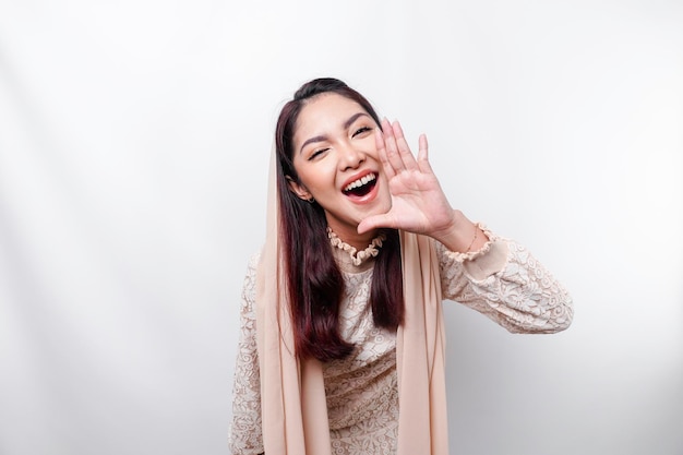 Jonge, mooie Aziatische moslimvrouw die een hoofddoek draagt en luid schreeuwt met een hand op haar mond communicatieconcept