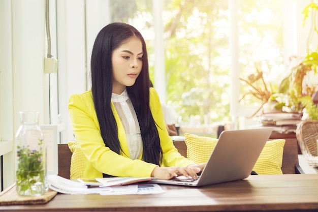 Jonge mooie Aziatische onderneemsterzitting bij lijst in koffiewinkel die met laptop werken