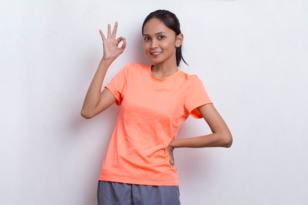 Jonge mooie aziatische sportieve vrouw die een duim omhoog ok gebaar toont op witte achtergrond