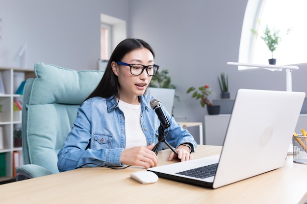 Jonge, mooie Aziatische vrouw die audiopodcastvrouw op kantoor opneemt met professionele microfoon