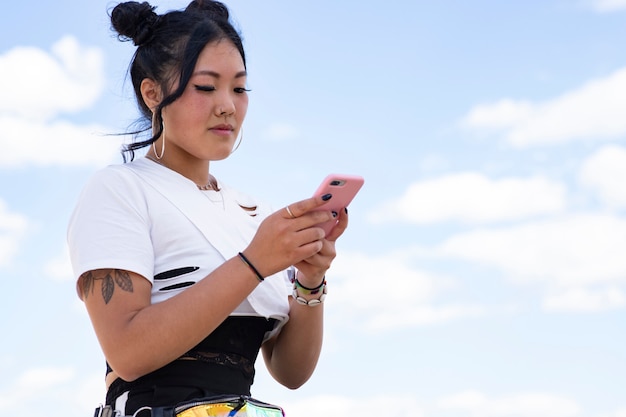 Jonge mooie aziatische vrouw die chirurgisch masker voor gezichtsbescherming draagt die een smartphone in het park gebruikt