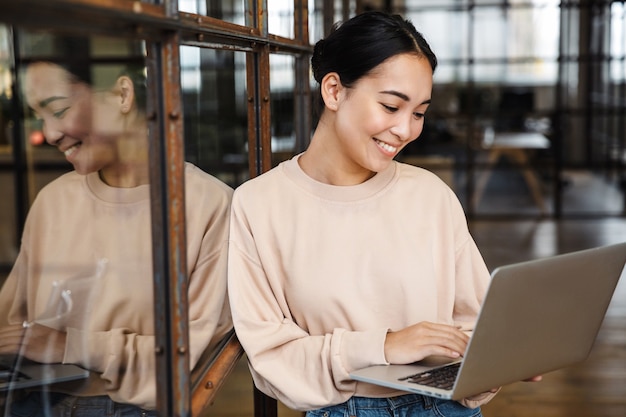 jonge mooie aziatische vrouw die lacht en een laptop vasthoudt terwijl ze op kantoor werkt