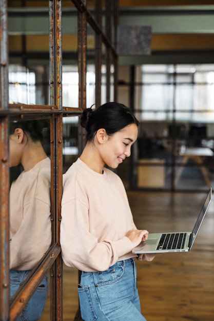 jonge mooie aziatische vrouw die lacht en een laptop vasthoudt terwijl ze op kantoor werkt