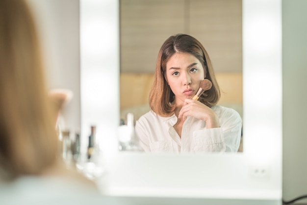 Jonge mooie Aziatische vrouw die make-up in de buurt van spiegel