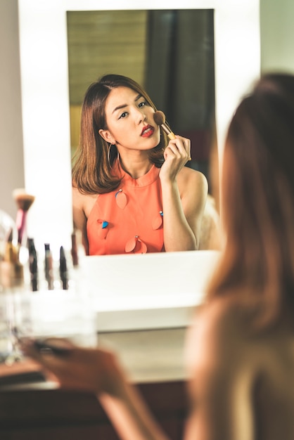 Jonge mooie Aziatische vrouw die make-up in de buurt van spiegel