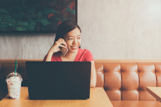 Jonge mooie Aziatische vrouw die met laptop op de achtergrond van de koffiewinkel werken met uitstekende filter