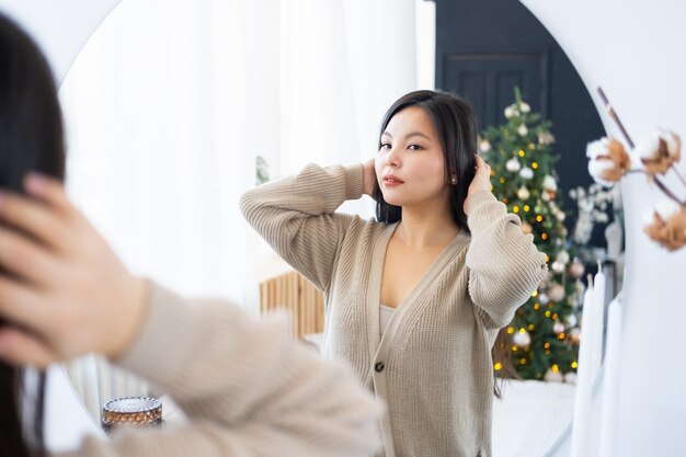 Jonge mooie aziatische vrouw die naar haar spiegelbeeld in de spiegel kijkt en glimlacht