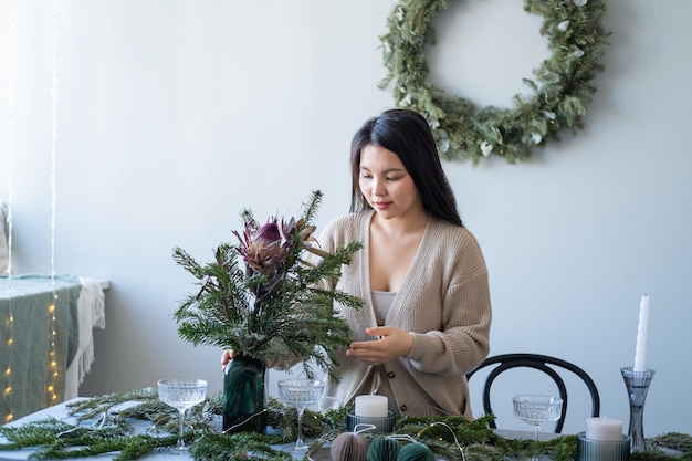 Jonge mooie aziatische vrouw die tafel decoreert met kerstboomtakken en kaarsen