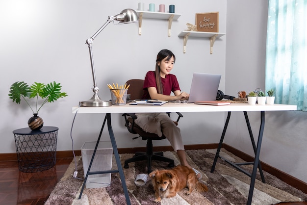 Jonge mooie Aziatische vrouw die thuis met haar hond werkt