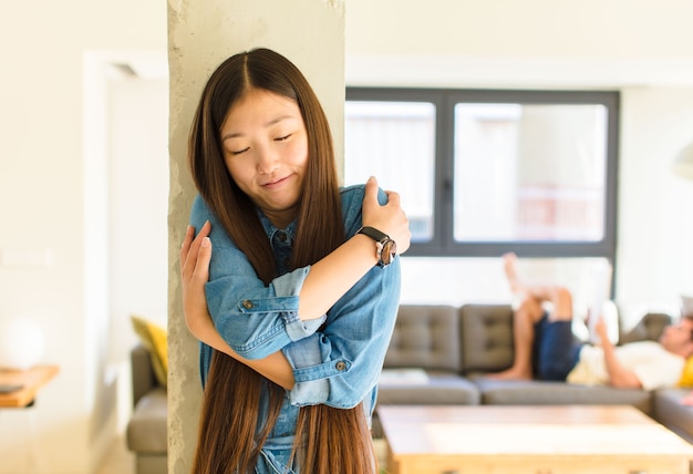 Jonge mooie aziatische vrouw die verliefd is, glimlachend, knuffelt en zichzelf knuffelt, vrijgezel blijft, egoïstisch en egocentrisch is