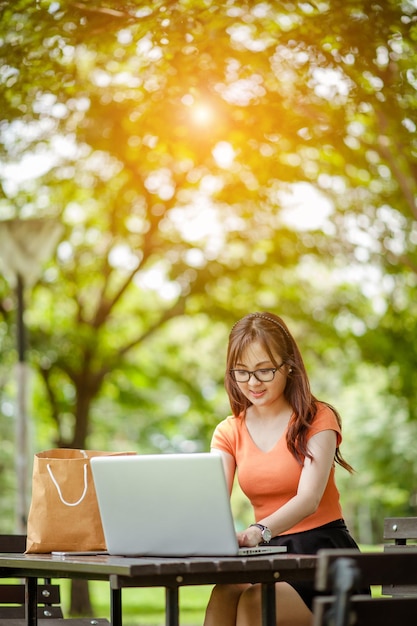 Jonge mooie Aziatische vrouw die werkt met laptop internet online winkelen in het buitenpark glimlach fris en gelukkig ontspannend gevoel in de ochtend freelancer werkend zakenvrouw lifestyle concept