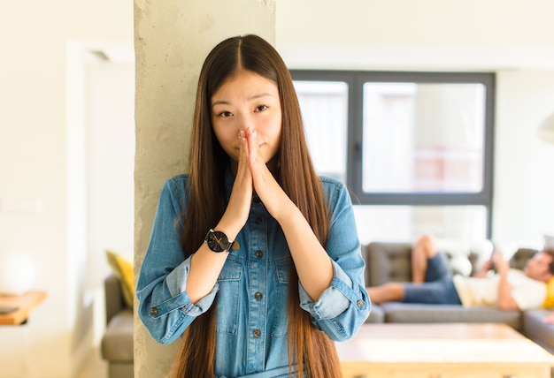 Jonge mooie Aziatische vrouw die zich bezorgd, hoopvol en religieus voelt, trouw bidt met de handpalmen ingedrukt, om vergeving smeekt