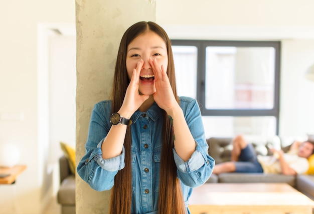 Jonge mooie Aziatische vrouw die zich gelukkig, opgewonden en positief voelt, een grote schreeuw geeft met handen naast de mond, roept