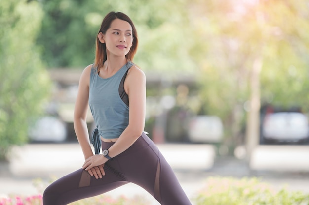 Jonge, mooie Aziatische vrouw in sportoutfits die zich uitstrekt voor het sporten tijdens de COVID-19-pandemie om een gezond leven te houden. Gezonde jonge vrouw die zich uitstrekt en zich opwarmt voor trainingen