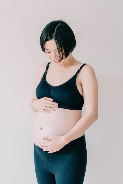 Jonge mooie Aziatische zwangere vrouw wat betreft haar buik thuis