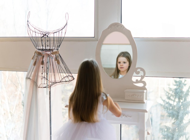 jonge mooie balletballerina zit op een poef voor een spiegel. Kleine meid