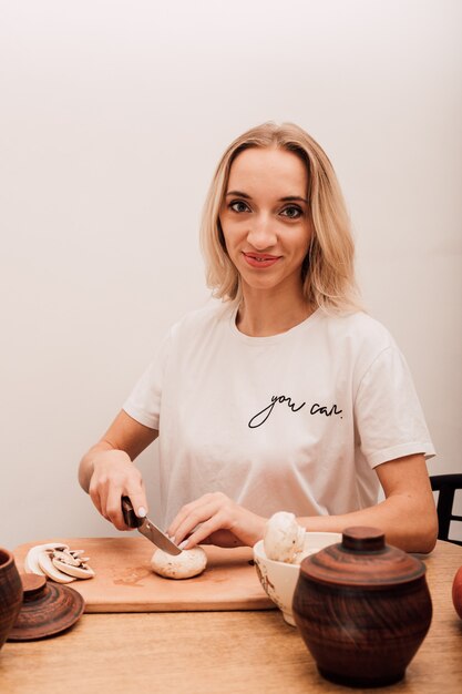 Jonge mooie blonde snijdt champignons op tafel in de keuken