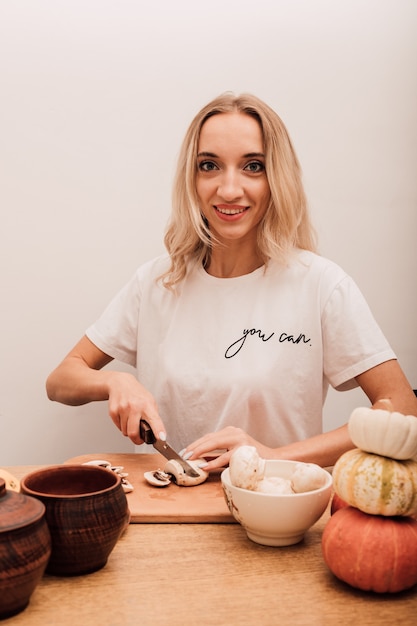 Jonge mooie blonde snijdt champignons op tafel in de keuken