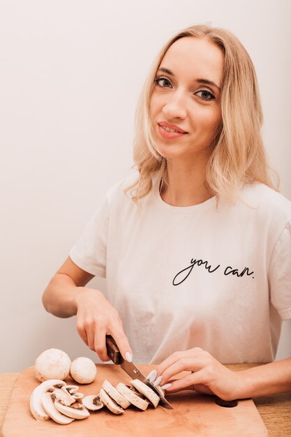 Foto jonge mooie blonde snijdt champignons op tafel in de keuken