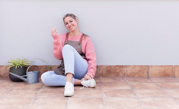 Jonge mooie blonde tuinman vrouw zittend op de vloer met een kopie ruimte aan de zijkant