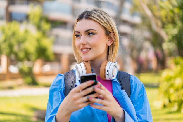Jonge mooie blonde vrouw buiten met een mobiele telefoon