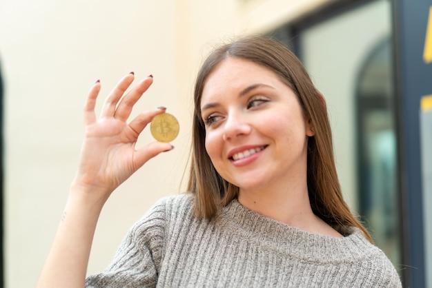 Jonge mooie blonde vrouw die een Bitcoin vasthoudt en ernaar kijkt