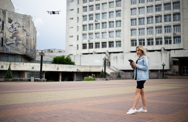 Jonge mooie blonde vrouw die een drone bestuurt met een afstandsbediening in haar hand