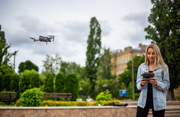 Jonge mooie blonde vrouw die een drone bestuurt met een afstandsbediening in haar hand