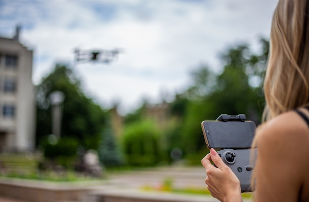 Jonge mooie blonde vrouw die een drone bestuurt met een afstandsbediening in haar hand