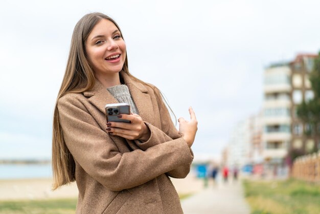 Jonge mooie blonde vrouw die mobiele telefoon gebruikt en terug wijst