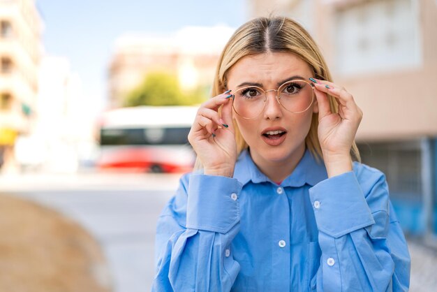 Foto jonge mooie blonde vrouw in de buitenlucht met bril en gefrustreerde uitdrukking