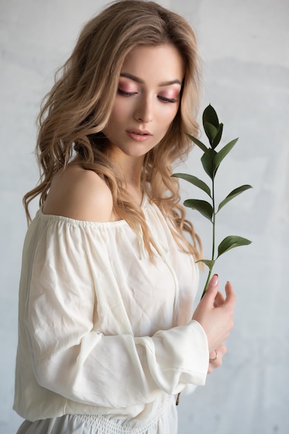 Jonge mooie blonde vrouw in een witte jurk met een bloem in haar handen. Mode portret close-up